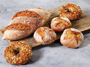 Ein Brot, drei Brötchen und zwei Bagels aus IREKS PROTEIN BREAD liegen angerichtet auf einem Brett